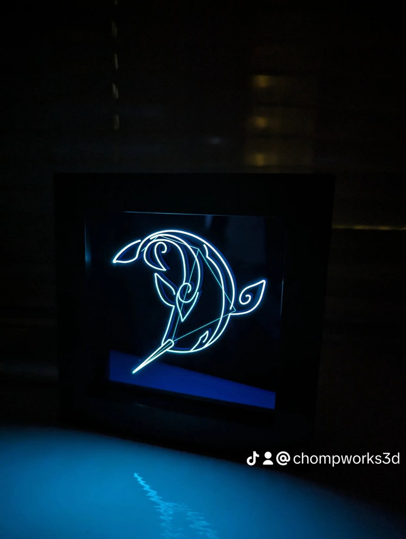May include: A black framed light-up wall art piece with a white outline of a narwhal. The narwhal is facing left and has a long, thin horn. The background is black. The text "@chompworks3d" is visible in the bottom right corner.