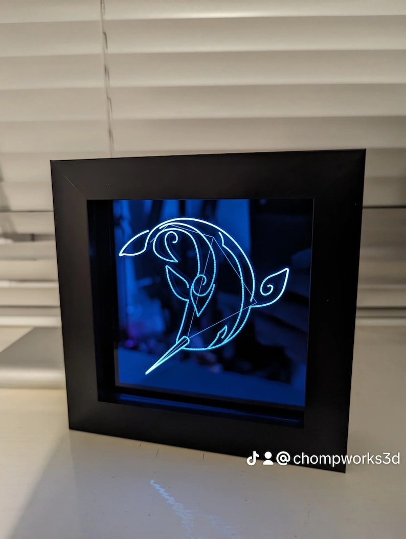 May include: A black framed 3D light sculpture of a stylised dolphin with a blue background. The light sculpture is lit up with a blue light. The TikTok handle @chompworks3d is visible in the bottom right corner of the image.