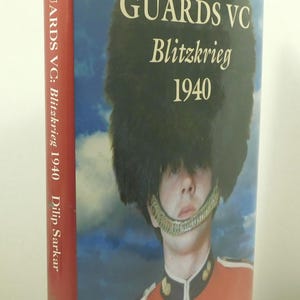 May include: A hardcover book titled GUARDS VC Blitzkrieg 1940 by Dilip Sarkar. The cover features a soldier in a red uniform and a tall black bearskin hat against a blue sky. The spine is red with white text, and the front cover displays the title.