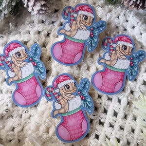 May include: Four stickers of a lizard in a Santa hat and a Christmas stocking. The pink stocking has a white cuff and blue trim. The lizard is tan and green. The stickers are surrounded by Christmas greenery and pine cones.