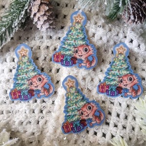 May include: Four Christmas tree-shaped stickers featuring a cartoon lizard holding a present. Each sticker has a decorated Christmas tree with a star. The stickers are on a white, textured surface with pine branches.