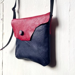 May include: A small, red and black leather crossbody bag with a button closure. The bag has a flap on the front and a long strap.