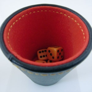 May include: A black leather dice cup with a red felt interior. Four orange dice are inside the cup.