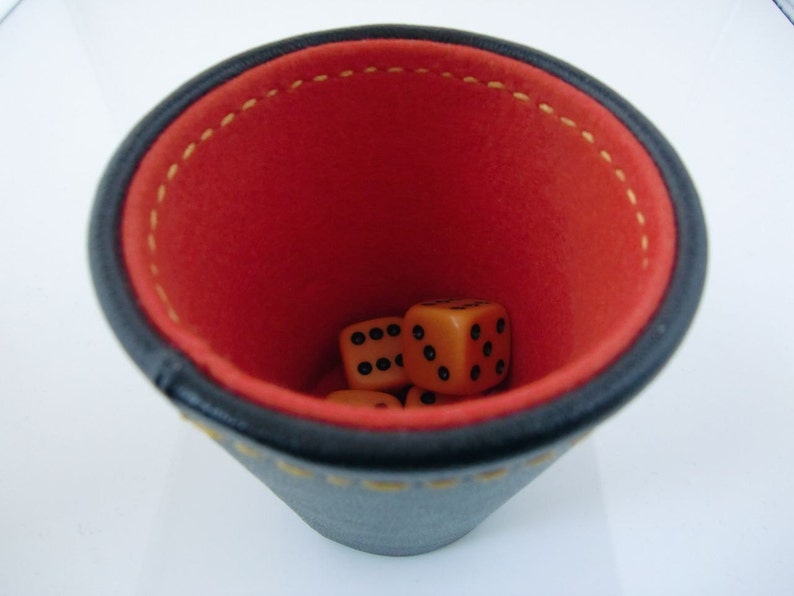 May include: A black leather dice cup with a red felt interior. Four orange dice are inside the cup.