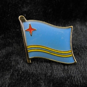 Könnte beinhalten: Eine goldfarbene Anstecknadel mit einem blauen, gelben und roten Flaggenmotiv. Die Flagge hat einen roten Stern in der oberen linken Ecke und zwei gelbe Streifen auf blauem Hintergrund.