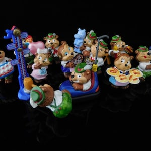 May include: A collection of 14 small, colorful figurines of bears wearing traditional German clothing. The figurines are made of plastic and have a variety of poses and expressions. Some of the bears are holding food, such as pretzels and sausages, while others are holding musical instruments. The figurines are all standing on a black surface.