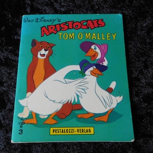 Peut inclure: Un livre vintage d'Aristochats de Walt Disney mettant en scène Tom O'Malley, un chat roux, et deux oies blanches. La couverture du livre est bleu turquoise avec du texte jaune et une bordure blanche. Le texte indique "Walt Disney's Aristocats Tom O'Malley" et "Pestalozzi-Verlag".