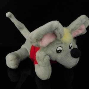 Könnte beinhalten: Ein graues Plüschmaus-Spielzeug mit einem roten Shirt und gelbem Haar. Die Maus hat rosa Ohren und eine schwarze Nase.