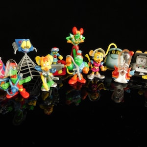 Könnte beinhalten: Eine Sammlung von 11 bunten Plastikfiguren, darunter eine Spinne, ein Roboter, eine Kreatur mit grünem Körper und rotem Hut und eine Kreatur mit rotem Körper und gelbem Hut. Die Figuren stehen alle auf einer schwarzen Oberfläche.