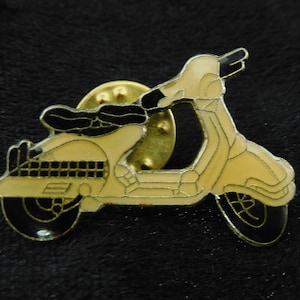 Könnte beinhalten: Eine goldfarbene Metallstifte mit einem gelben Roller mit schwarzen Details. Der Roller hat einen schwarzen Sitz und schwarze Räder.