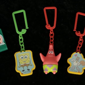 Puede incluir: Cuatro llaveros con personajes de Bob Esponja. Los llaveros representan a Bob Esponja, Patricio Estrella, Gary el Caracol y Arenita. Los llaveros son de plástico y tienen un esquema de color amarillo, verde, rojo y azul.