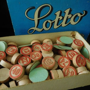 Könnte beinhalten: Eine Nahaufnahme einer Kartonbox gefüllt mit roten und weißen nummerierten Holzmarken. Die Box ist mit "Lotto" in blauer Kursivschrift beschriftet.