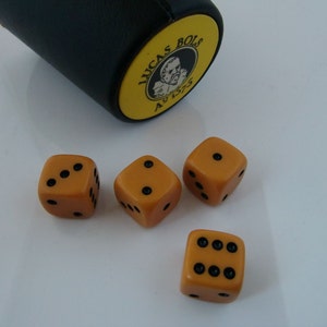 May include: Four orange dice with black dots on a white surface. The dice are next to a black and yellow dice cup with the text "Lucas Bols 1575" on it.