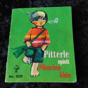 Peut inclure: Une couverture de livre verte avec une illustration colorée d'un garçon tenant une fleur. Le titre est "Pitterle spielt Hänschen klein" et le numéro "Nr. 109" est imprimé dans le coin inférieur gauche.
