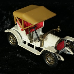 Puede incluir: Un coche de juguete blanco con una capota de tela de color beige y un interior rojo. El coche tiene un volante dorado y detalles dorados.