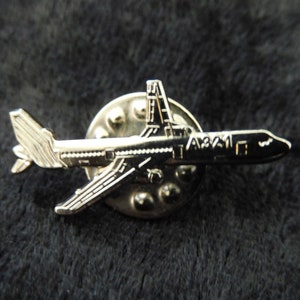 Könnte beinhalten: Silberne Flugzeugnadel mit detailliertem Design und dem Text "A321" an der Seite.