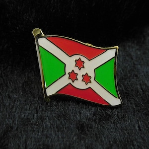 Könnte beinhalten: Eine goldfarbene Anstecknadel mit der Flagge von Burundi. Das Flaggen-Design umfasst rote und grüne Abschnitte, weiße diagonale Streifen und drei rote Sterne. Die Anstecknadel hat eine glänzende, polierte Oberfläche.