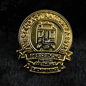 Könnte beinhalten: Goldfarbener Pin mit dem Text "West Coast Railway Association Preserving British Columbia's Railway Heritage" um eine Darstellung eines Eisenbahnwagens.