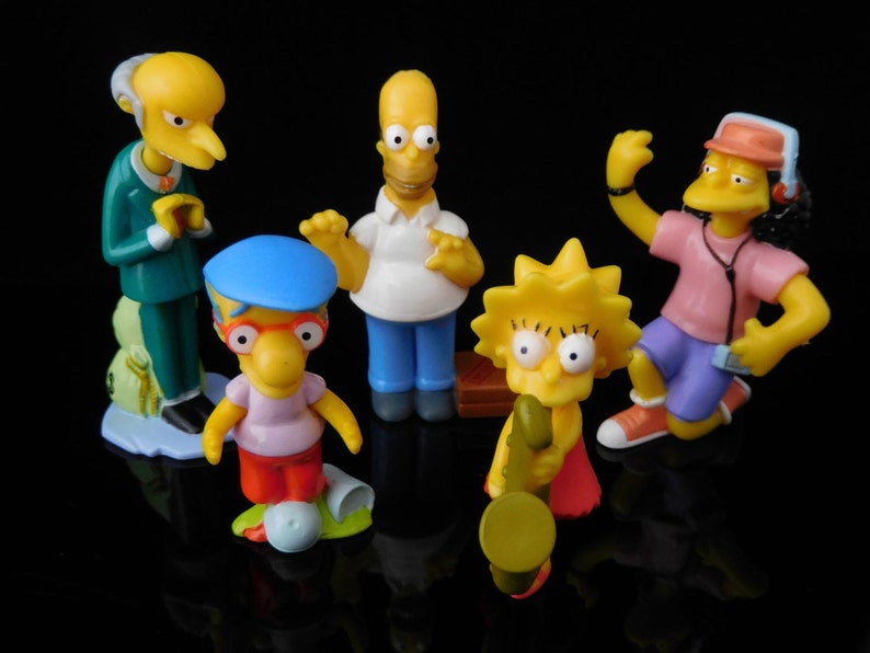 Pode incluir: Um conjunto de seis figuras de pl&aacute;stico amarelo de personagens do programa de televis&atilde;o animado Os Simpsons. Os personagens incluem Homer, Marge, Bart, Lisa, Maggie e Krusty, o Palha&ccedil;o. As figuras est&atilde;o todas em poses diferentes e usam suas roupas caracter&iacute;sticas.