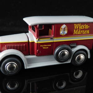 Może przedstawiać: Czerwono-szary, zabawkowy samochód dostawczy z białą kabiną i czerwoną skrzynią ładunkową. Samochód ma żółty pasek i napis "Wiesn-Märzen" nadrukowany na boku. Samochód ma czarne koła i srebrne kołpaki.