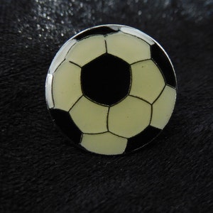 Könnte beinhalten: Eine schwarze und weiße Emaille-Fußball-Anstecknadel. Der Ball ist hellgelb mit schwarzen Nähten und einem schwarzen Mittelfeld.