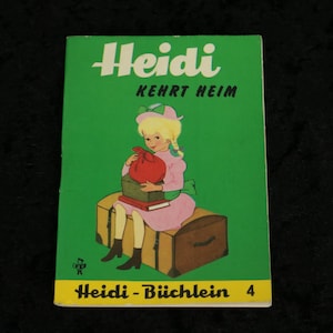 Puede incluir: Una portada de libro infantil vintage con una ni&ntilde;a de pelo rubio y un vestido rosa sentada en un cofre de madera. El t&iacute;tulo del libro es "Heidi Kehrt Heim" y el subt&iacute;tulo es "Heidi - B&uuml;chlein 4".