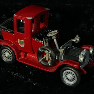 Puede incluir: Un coche de juguete rojo con ruedas negras y una capota de tela negra. El coche tiene un motor detallado y un volante.