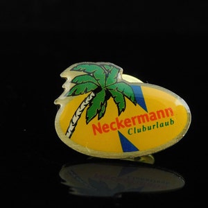 Könnte beinhalten: Eine gelbe und blaue Emaille-Anstecknadel mit einer Palme und dem Text "Neckermann Cluburlaub".
