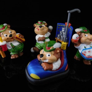 May include: Set of five colorful figurines of bears wearing traditional German clothing. The bears are holding various items, including a hot dog, a soda, a basket of eggs, and a car.