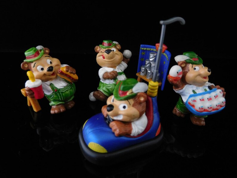 May include: Set of five colorful figurines of bears wearing traditional German clothing. The bears are holding various items, including a hot dog, a soda, a basket of eggs, and a car.