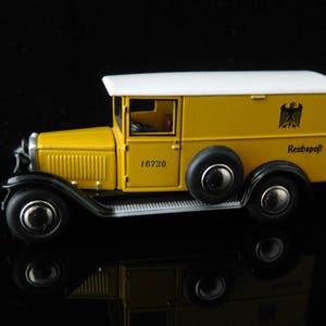 May include: A yellow toy delivery truck with a white roof and a black German eagle logo. The truck has the words "Reichspost" and "16730" printed on the side.