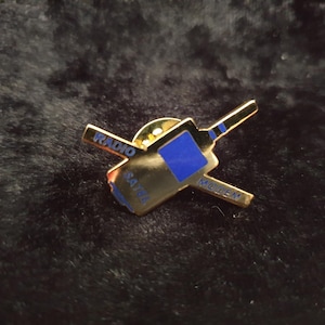 Könnte beinhalten: Goldfarbener Pin mit einer blauen und weißen Illustration eines Mobiltelefons mit den Worten "RADIO SATEL" und "MODERN" an den Seiten.