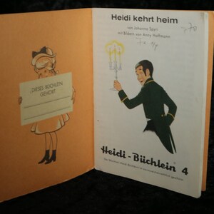 Puede incluir: Una portada de libro vintage para "Heidi kehrt heim" de Johanna Spyri, ilustrada por Anny Hoffmann. La portada presenta a una ni&ntilde;a sosteniendo un cartel que dice "DIESES BOCHLEIN GEHORT" y a un hombre con traje sosteniendo un candelabro. El libro es parte de la serie "Heidi-B&uuml;chlein", espec&iacute;ficamente el volumen 4.