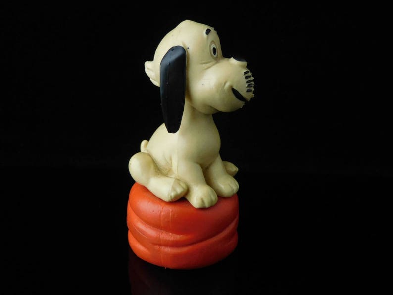 May include: A white and black dog figurine sitting on an orange cushion. The dog has a long snout and black ears.