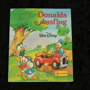 Könnte beinhalten: Ein Vintage-Kinderbuchcover mit Donald Duck und seinen Neffen. Das Cover ist mit Donald Duck illustriert, der ein rotes Auto fährt, in dem seine Neffen hinten sitzen. Der Titel des Buches lautet "Donalds Ausflug" und das Buch ist von Walt Disney.