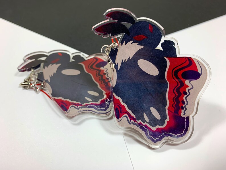 May include: Two clear acrylic charms featuring a black and white moth with red and purple accents. The moth has a skull-like face and large, black wings.