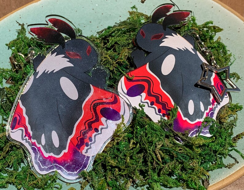 May include: Two black and white moth-shaped acrylic charms with red and purple wings. The charms have a star-shaped metal charm attached to them.