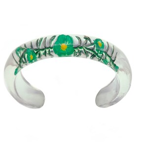 May include: A clear resin bangle bracelet with green and yellow flowers embedded inside.