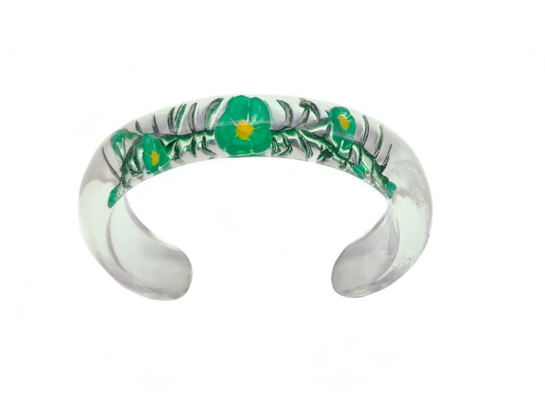 May include: A clear resin bangle bracelet with green and yellow flowers embedded inside.