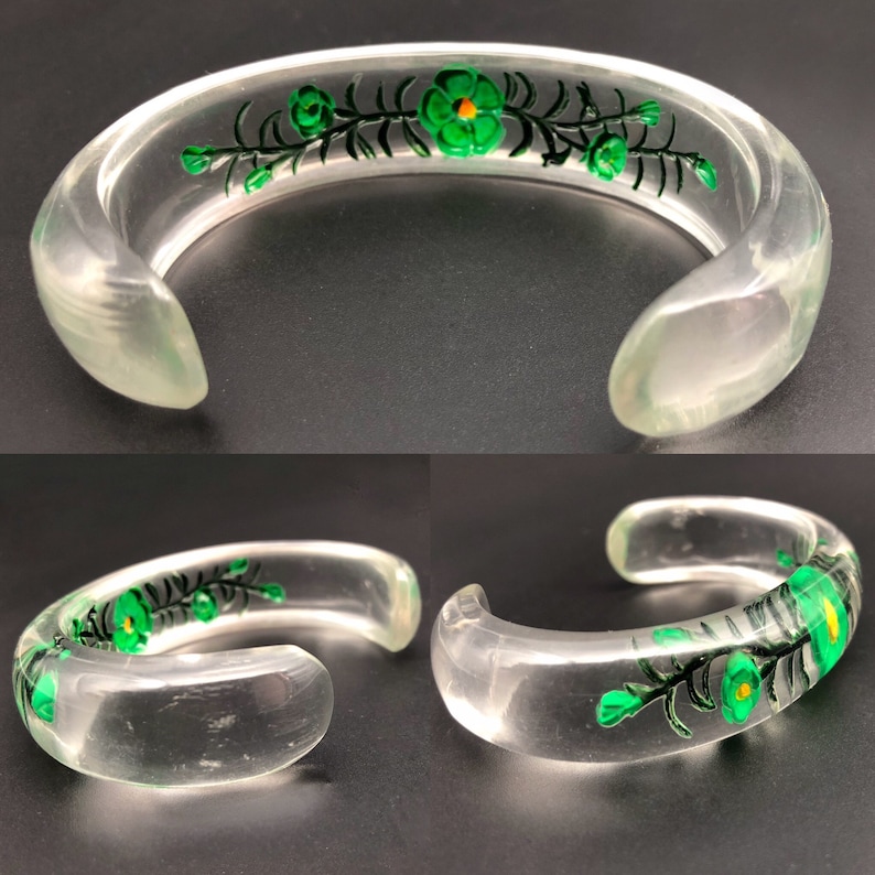 May include: A clear plastic bangle bracelet with a green floral design. The flowers have yellow centers and are painted on the bracelet.