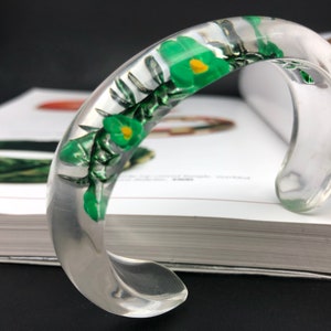 May include: A clear plastic bangle bracelet with green and yellow pressed flowers inside.