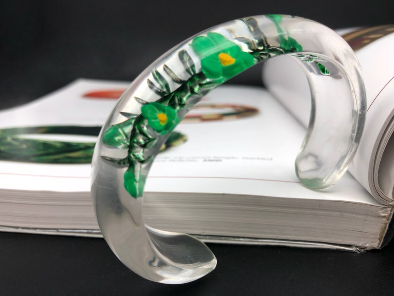 May include: A clear plastic bangle bracelet with green and yellow pressed flowers inside.