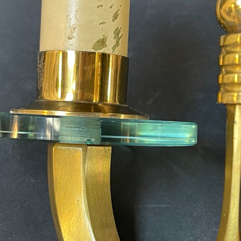 May include: Close-up of a brass candle holder with a clear, circular glass accent. The candle holder has a gold finish and a curved design. A partially burned candle is in the holder.