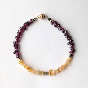 Könnte beinhalten: Ein Armband aus Granat- und Opal-Edelsteinen mit einem Magnetverschluss. Das Armband besteht aus kleinen, unregelmäßig geformten Steinen in den Farben Dunkelrot, Orange und Gelb.