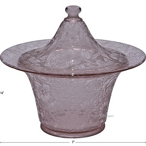May include: A pink glass covered dish with a floral design. The dish is 6 1/4 inches tall and 7 inches wide.