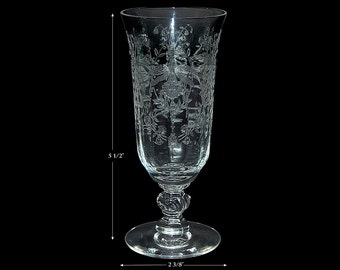 May include: A clear glass champagne flute with an etched floral design. The flute is 5 1/2 inches tall and 2 3/8 inches wide at the base.
