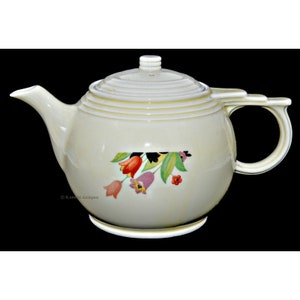 May include: A white ceramic teapot with a floral design featuring pink, red, and orange tulips. The teapot has a lid with a knob on top and a handle on the side.