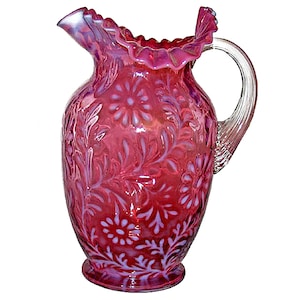 May include: A vintage cranberry glass pitcher with a ruffled top and a clear glass handle. The pitcher is decorated with a white floral pattern.