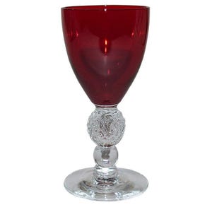 May include: A red wine glass with a clear, textured stem and base. The glass has a rounded bowl and a wide rim.