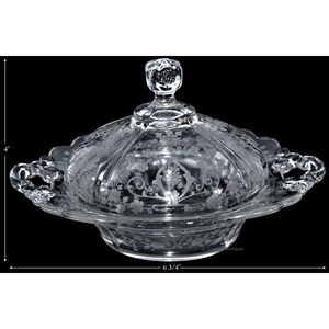 May include: A clear glass butter dish with a lid and two handles. The dish is decorated with an etched floral pattern. The dish measures 6 3/4 inches in diameter.